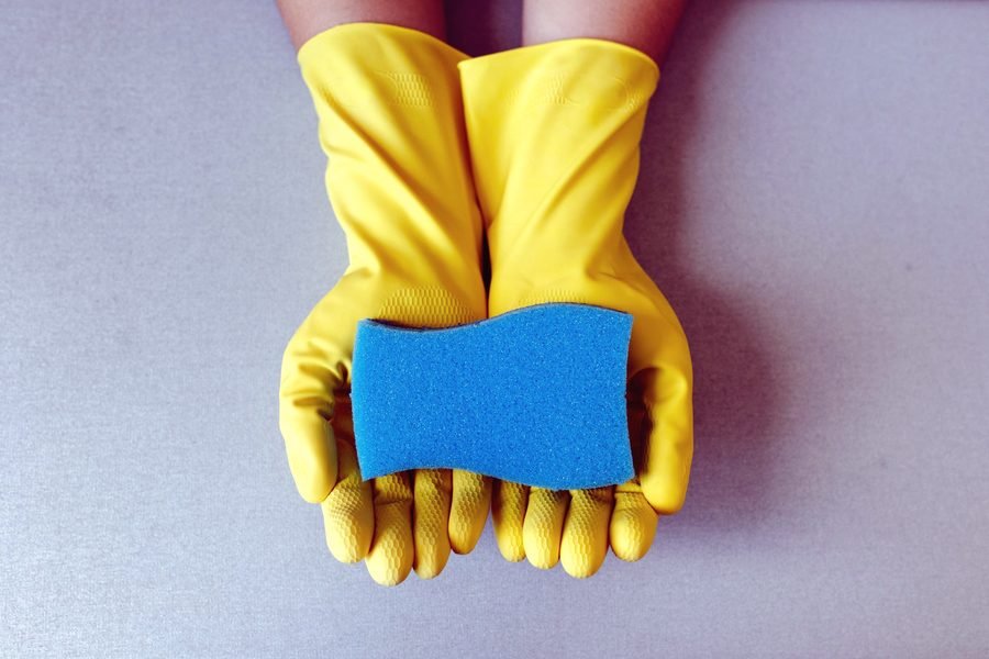 Yellow rubber gloves holding a cleaning sponge.