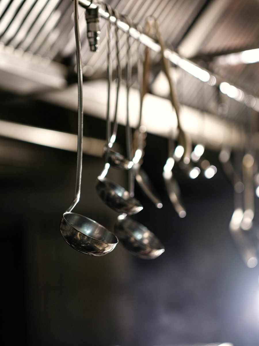 Stainless steel ladles hanging from an overhead rack in a professional kitchen.