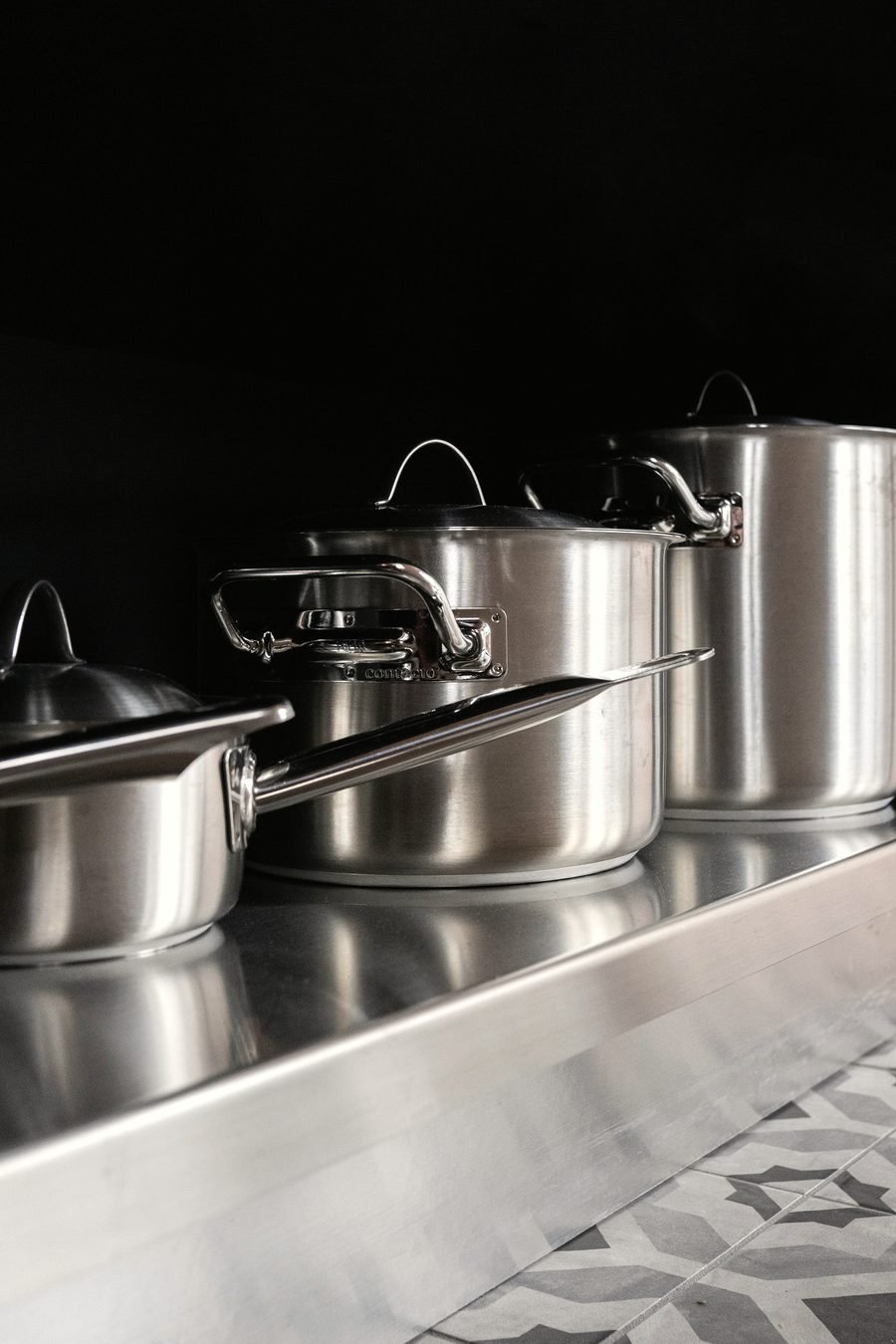 Stacked stainless steel stockpots with lids on a kitchen shelf.