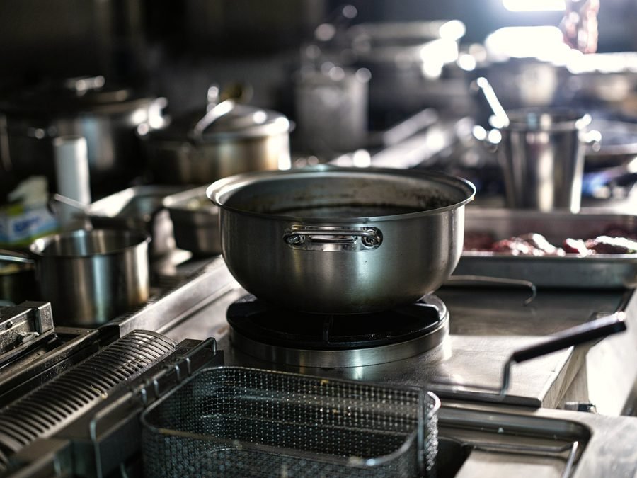 Stainless steel pots and a fry basket on a commercial kitchen range.