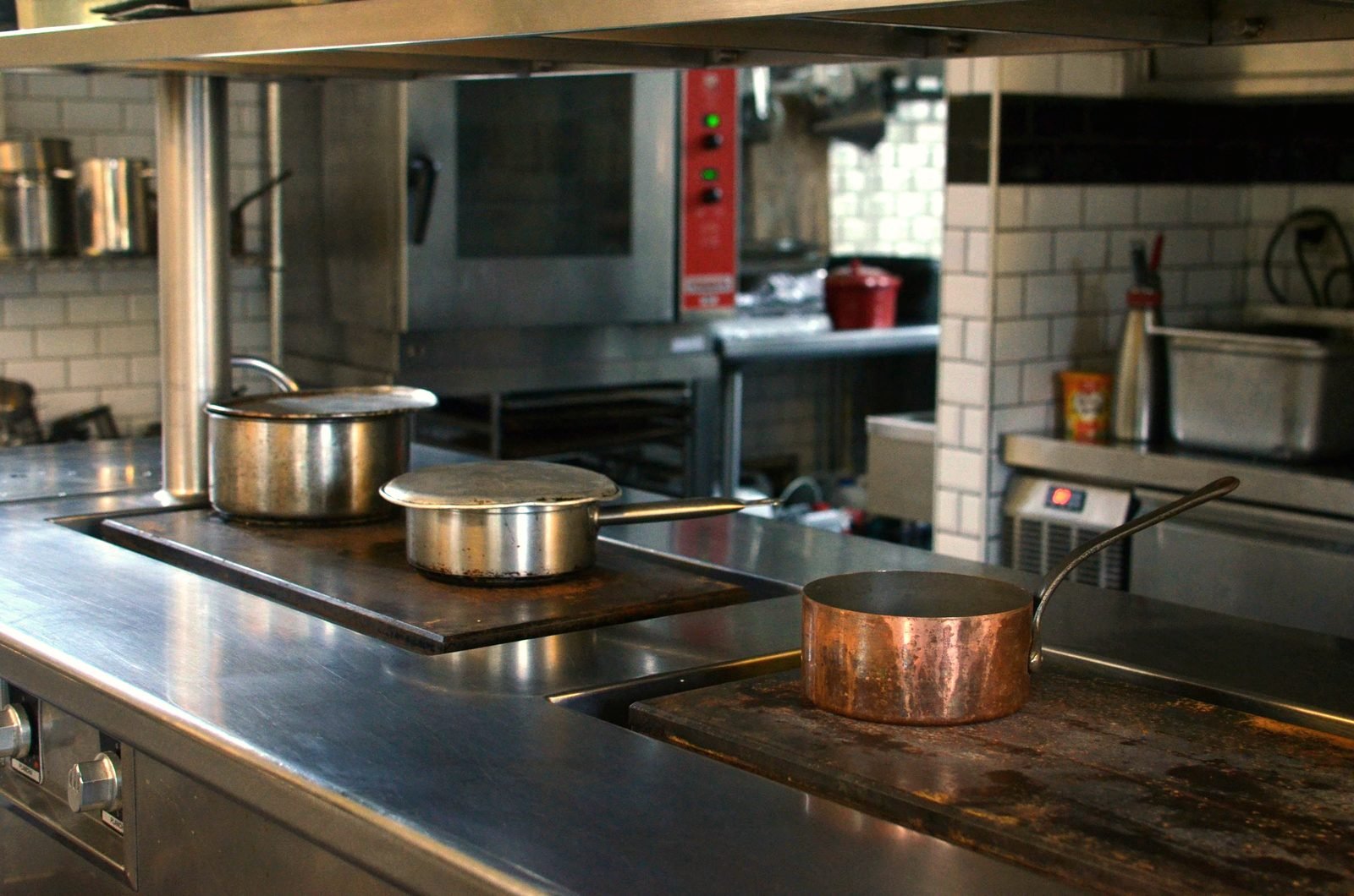 A stainless steel prep table and shelving in a commercial kitchen, tile backsplash behind it.