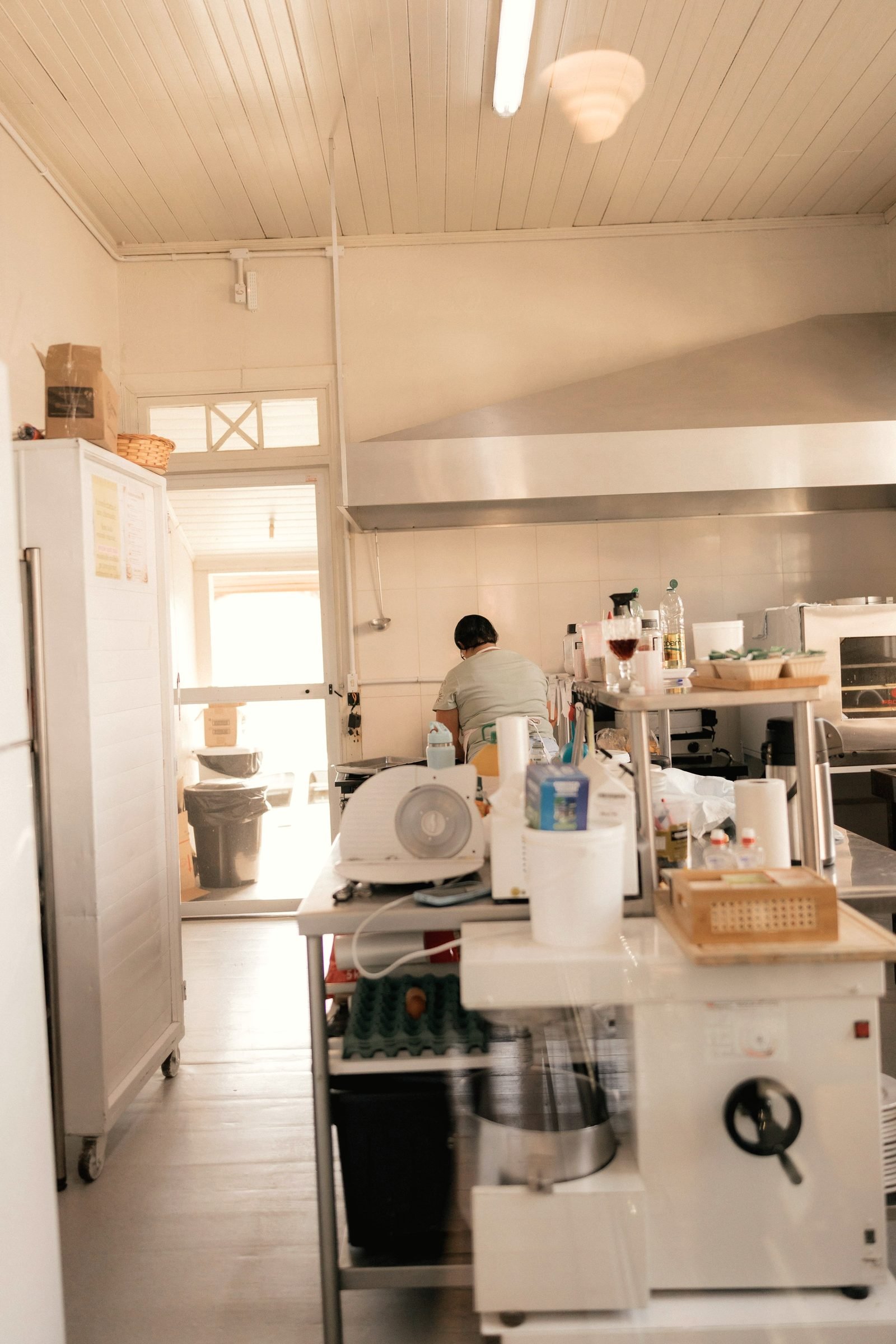 A kitchen worker at a prep station near an exhaust hood and steel shelving.