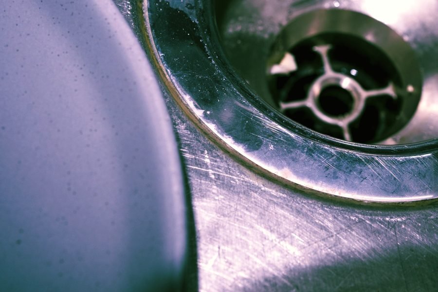 Macro view of a stainless steel sink drain and worn brass strainer ring.